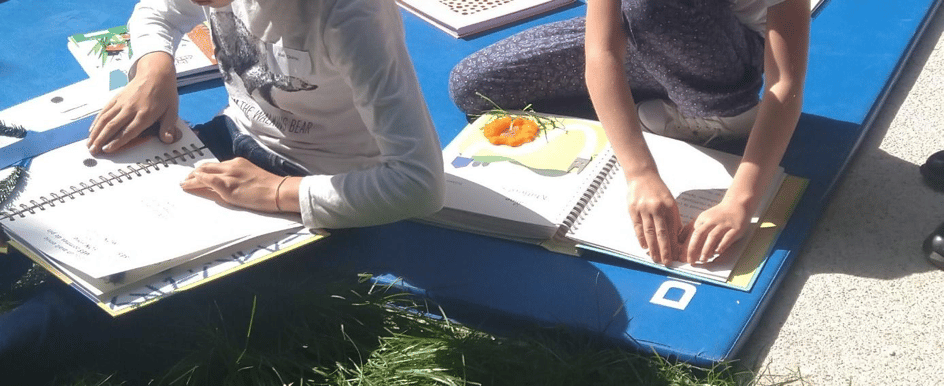 2 enfants dont on voit les mains posées sur le texte en braille de livres tactiles